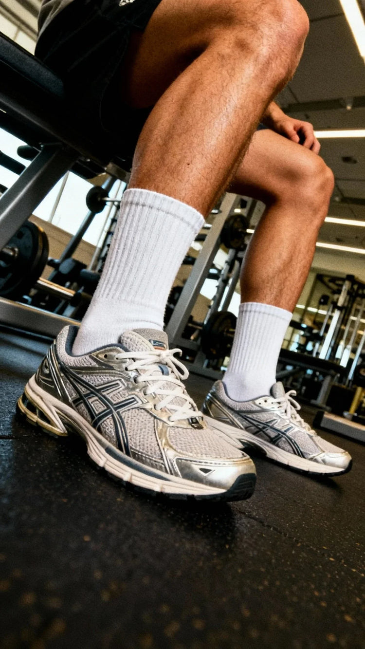 Close-up of legs wearing white crew socks and gray Asics running shoes in a gym setting