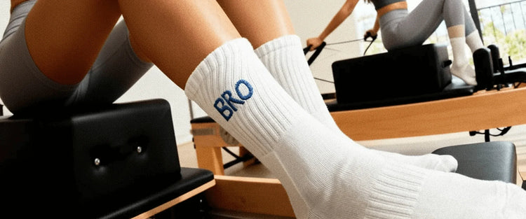 Close-up of legs wearing white socks with 'BRO' text during Pilates reformer workout